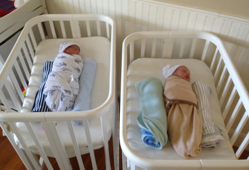 Max and Sam, swaddled in side by side, matching white Argington Bam Bassinets