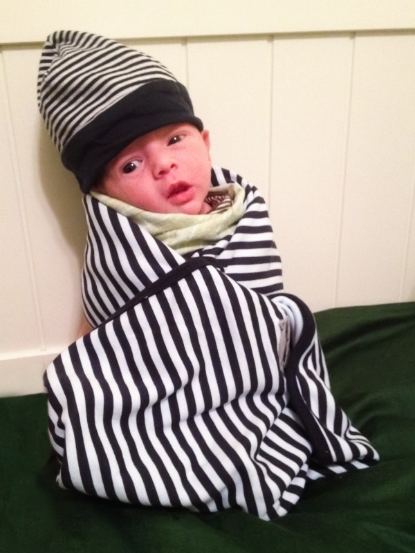 Baby boy Sam propped-up and wrapped in a striped blanket, wearing a striped hat