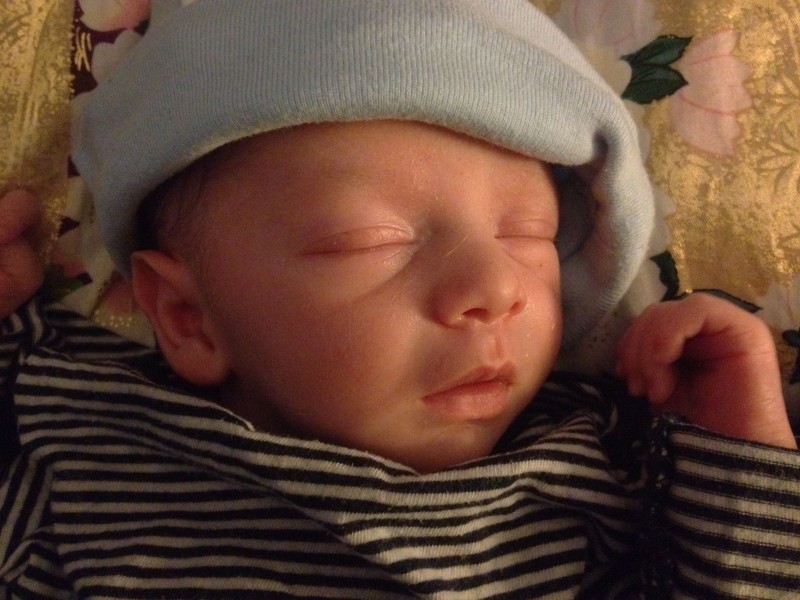 Baby boy Sam, asleep wearing a stripe shirt against a golden pillow. The tilt of his hat makes it look like a French beret.