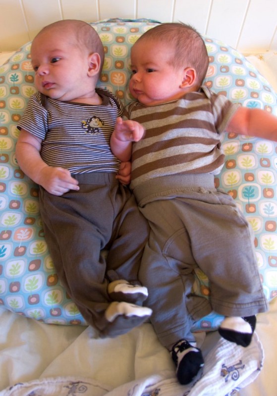 twin brothers, baby boys sam and max sit on a Boppy Newborn Lounger. Both are wearing pants and onesies.