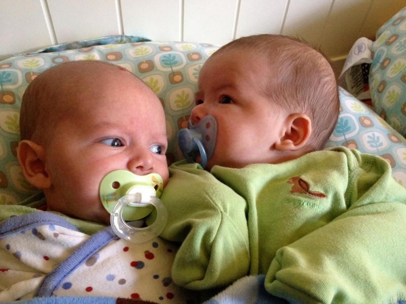 baby boys, twin brothers, sam and max, sit on a Boppy Newborn Lounger with pacifiers. Sam is swaddled, max is wearing a sweat-pea suit