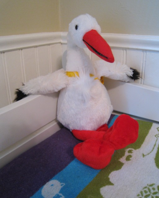 a stuffed stork sits smugly in the corner of a changing table