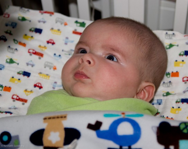 baby boy max sits in a Argington Bam bassinet with a Valboa blanket and burp cloth from Target covered in trains, planes, helicopters, trucks, and cars