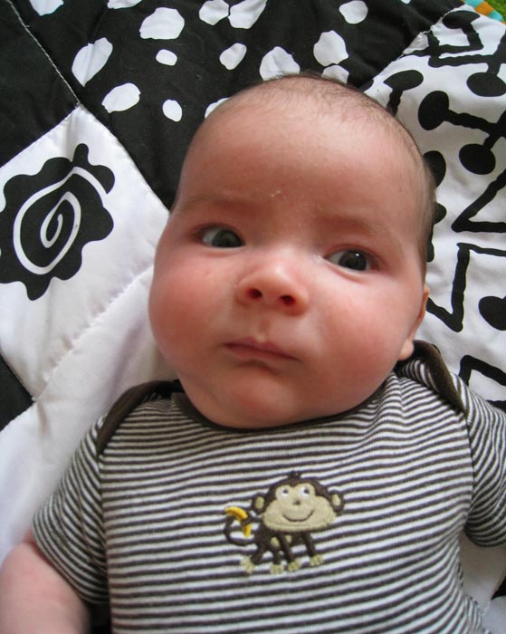 baby boy max, wearing a brown striped monkey onesie, lies on a black and white patterned baby blanket
