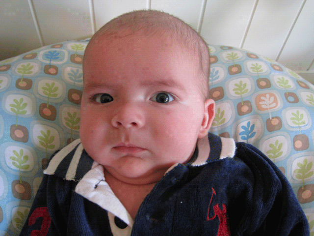 baby boy max wearing a polo outfit, sits on a Boppy Newborn Lounger and occasionally glances to the side. He has a cold.