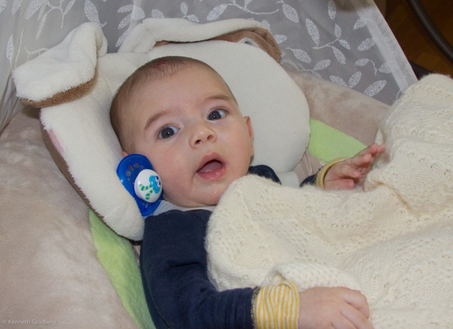 baby boy sam, sitting in a My Little Snugabunny Cradle'N'Swing, has a blue pacifier stuck next to his face